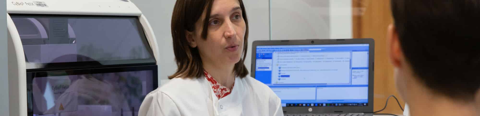 A person in a white lab coat speaking to a small group of people in a laboratory